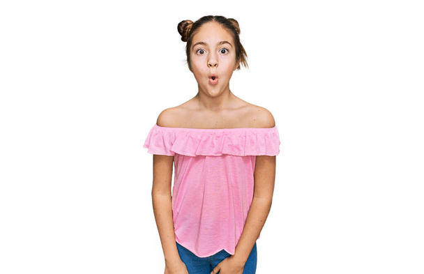 Piękna brunetka mała dziewczynka w letniej różowej koszuli przestraszony i zdumiony z otwartymi ustami dla zaskoczenia, niedowierzanie twarz  - Zdjęcie, obraz
