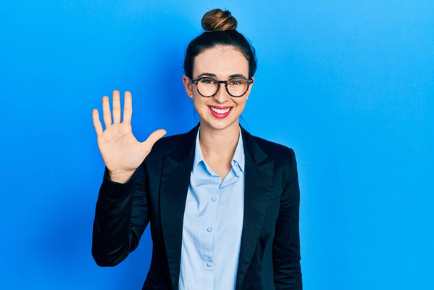 Joven chica hispana usando ropa de negocios y gafas mostrando y señalando con los dedos número cinco mientras sonríe confiada y feliz.  - Foto, Imagen
