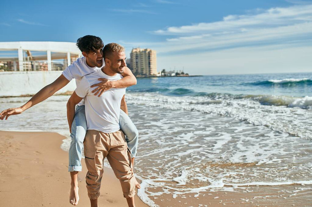 Милая гей-пара на прогулке на спине по пляжу. - Фото, изображение