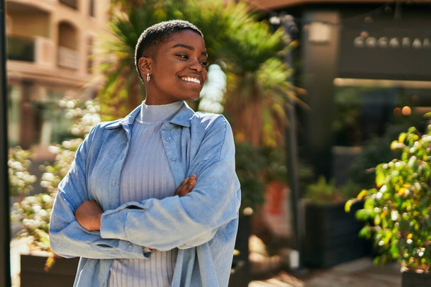 Młoda Afroamerykanka uśmiechnięta ze skrzyżowanymi ramionami w mieście. - Zdjęcie, obraz