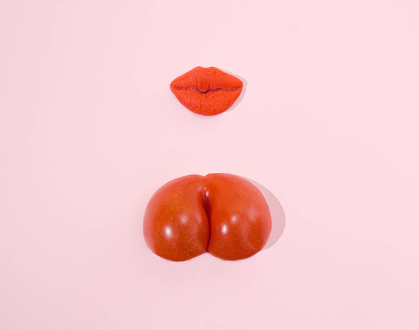 Lábios vermelhos e um tomate vermelho em fundo rosa pastel. Conceito criativo erótico. - Foto, Imagem