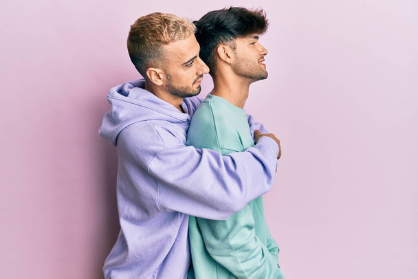 Гомосексуальна гей-пара, що стоїть разом в повсякденному одязі, дивлячись на бік, розслабляє профільну позу з природним обличчям і впевненою посмішкою
.  - Фото, зображення