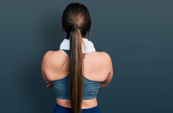 Młoda Latynoska ubrana w odzież sportową i ręcznik stojąca tyłem do siebie z skrzyżowanymi ramionami  - Zdjęcie, obraz