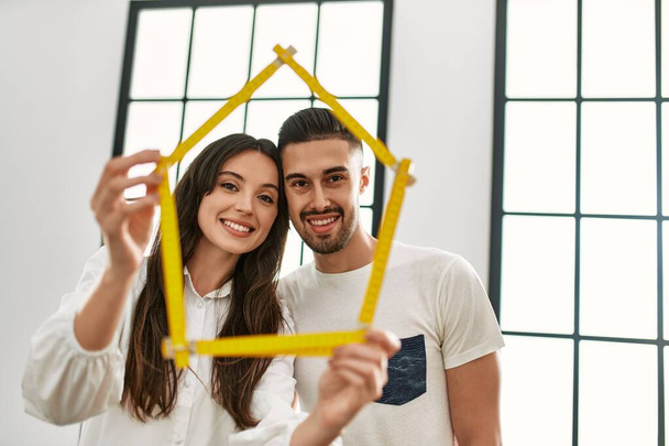 Νεαρό ζευγάρι ισπανόφωνων χαμογελά ευτυχισμένη εκμετάλλευση σπίτι έργο στο νέο σπίτι. - Φωτογραφία, εικόνα