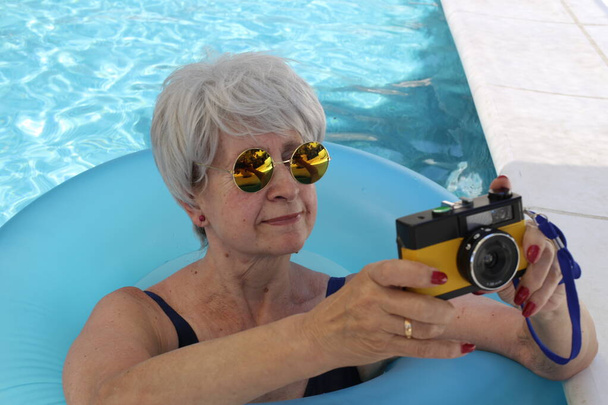 portré érett nő fürdőruhában gazdaság vintage film kamera medencében napsütéses nyári napon - Fotó, kép