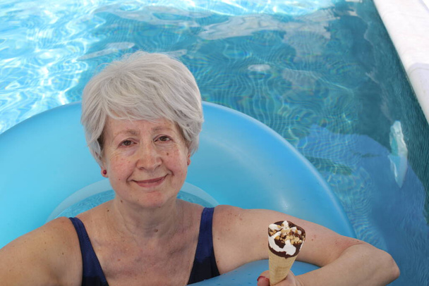 portré érett nő fürdőruhában felfújható cső eszik jégkrém medencében a napos nyári napon - Fotó, kép
