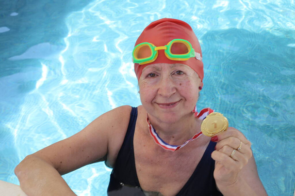 portrait of mature woman in swimsuit with golden medal in pool on sunny summer day - Photo, Image