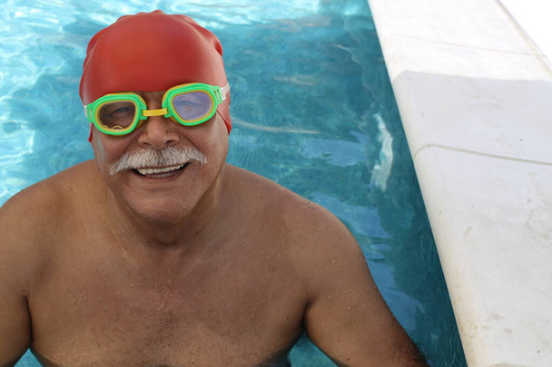 portrait of mature man with rubber swimming hat and goggles in pool on sunny summer day - Photo, Image