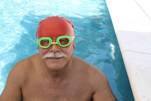 portrait of mature man with rubber swimming hat and goggles in pool on sunny summer day - Foto, Imagem