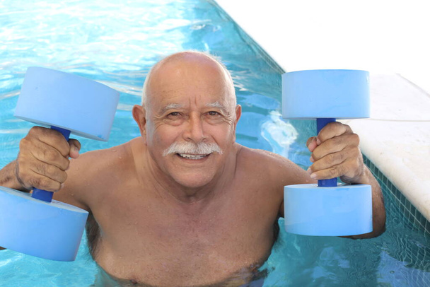 portré érett férfi gazdaság aqua aerobic harangok medencében napsütéses nyári napon - Fotó, kép