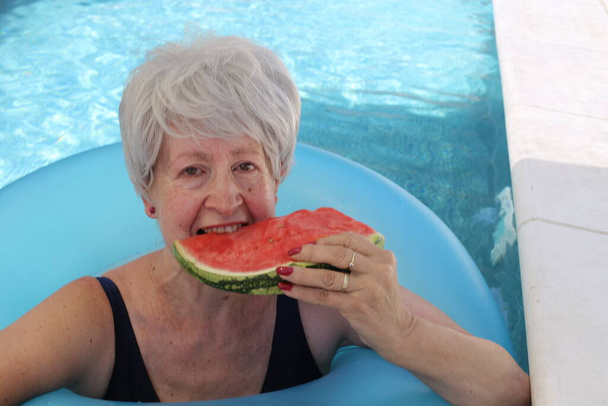 portré érett nő fürdőruhában szelet görögdinnye medencében a napos nyári napon - Fotó, kép