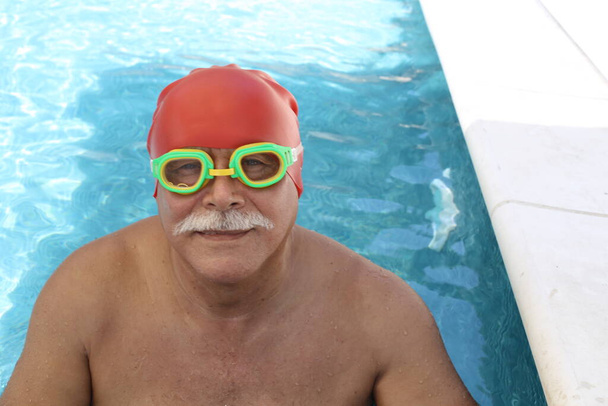 portrait of mature man with rubber swimming hat and goggles in pool on sunny summer day - Zdjęcie, obraz