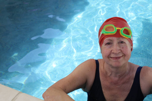 Porträt einer reifen Frau im Badeanzug mit Badehut und Brille im Pool an einem sonnigen Sommertag - Foto, Bild