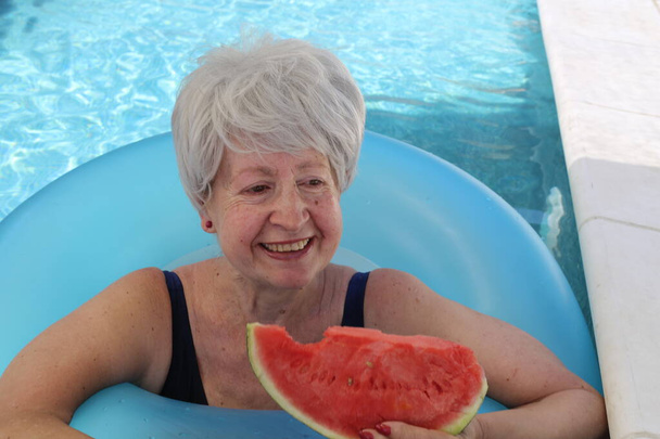 portré érett nő fürdőruhában szelet görögdinnye medencében a napos nyári napon - Fotó, kép