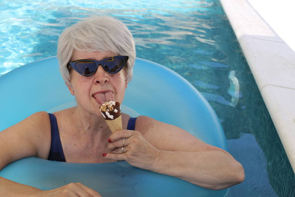 portré érett nő fürdőruhában felfújható cső eszik jégkrém medencében a napos nyári napon - Fotó, kép