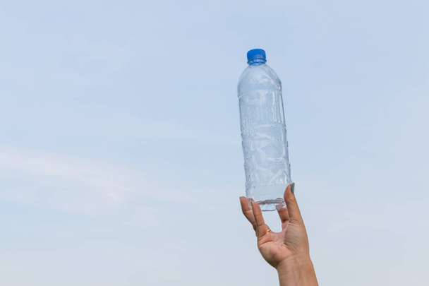 Nő kéz fogja üveg ivóvíz egy kék ég háttér - Fotó, kép