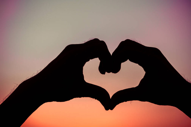 Liebeszeichen. Herz-Symbol von Hand Silhouette in Sonnenuntergang Himmel. Hintergrund im Vintage-Stil - Foto, Bild