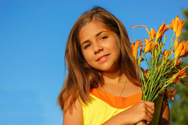 Красивая счастливая девочка-подросток в желтом платье с букетом апельсинов на фоне голубого неба в солнечный летний день. Девочка, 10-12 лет. 1 сентября, возвращение в школу, День матери. - Фото, изображение
