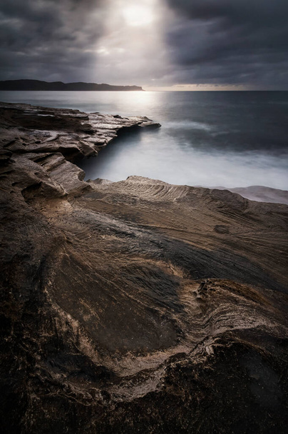 Light pouring down onto the rocks and the ocean on the coast - Photo, Image