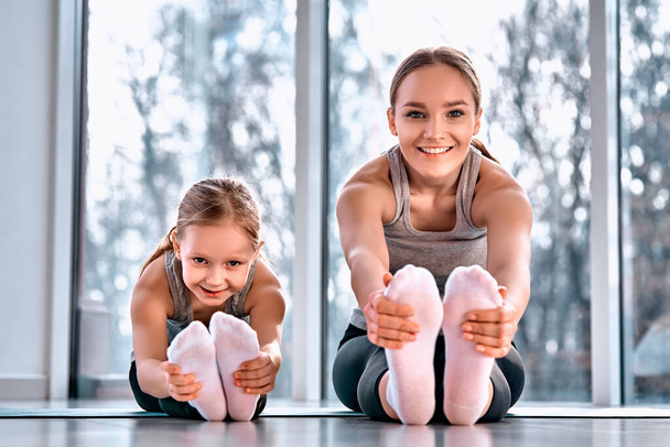 Mom and daughter do stretching before exercise. Family in bright, modern spacious yoga center - Fotoğraf, Görsel