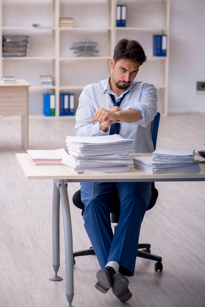 Jonge mannelijke werknemer ongelukkig met overmatig werk in het kantoor - Foto, afbeelding