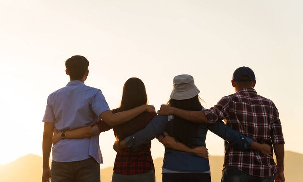 Group of happy friends are having fun with holding together in front of mountain and enjoy sunset showing unity and teamwork. Friendship happiness leisure partnership team concept. - Foto, afbeelding