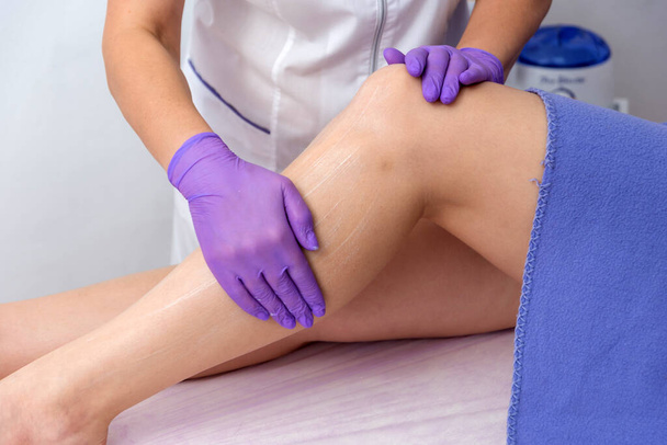 Косметическая процедура нанесения крема на эпиляцию ног, растирание крема, смягчение кожи - Фото, изображение