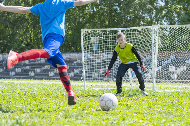 若いサッカーのゴールキーパーは投げる準備ができて、ジャンプのフィールドプレーヤーはゴールで打つ. - 写真・画像