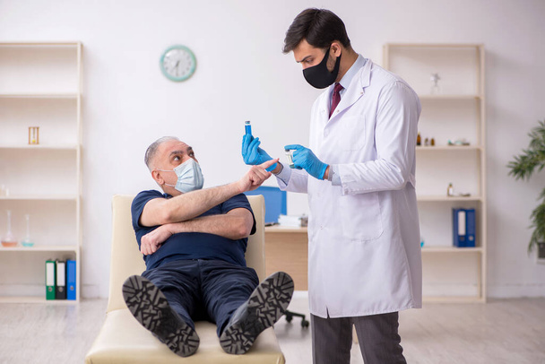 Paciente do sexo masculino idoso visitando jovem médico do sexo masculino em conce vacinação - Foto, Imagem