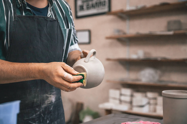 A closeup of a person polishing a clay pot on the table in a workshop - Foto, Imagem