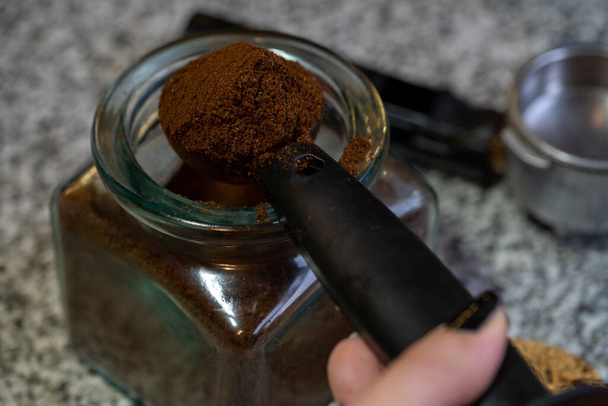 A closeup shot of a female hand taking ground coffee from a glass jar with a plastic spoon - Zdjęcie, obraz