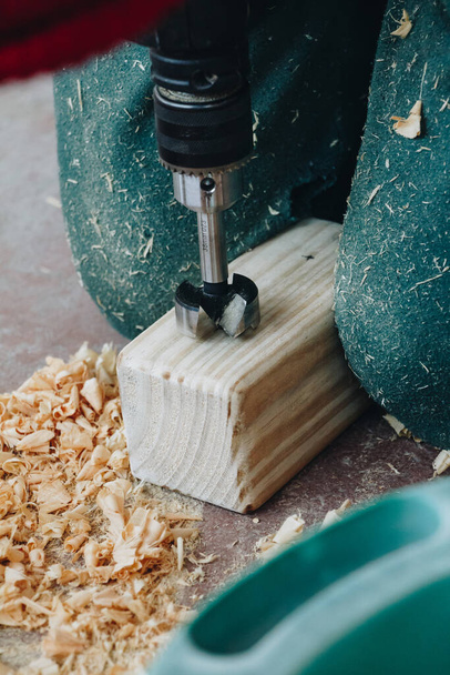 A vertical shot of a person drilling a hole in a small wooden cuboid in a workshop - Foto, imagen