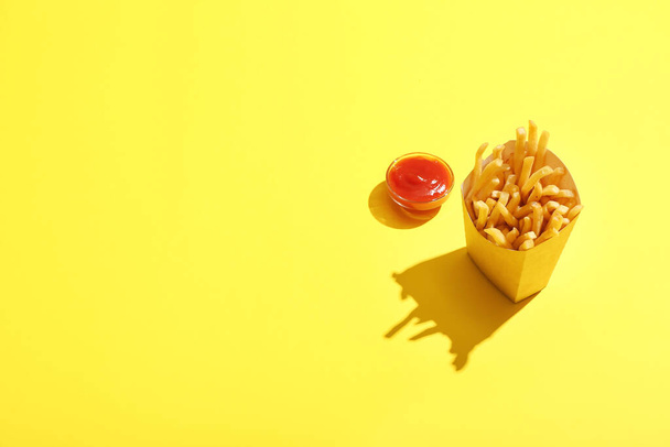 Paper box with tasty french fries and tomato sauce on color background - Φωτογραφία, εικόνα