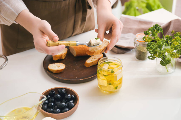 Mujer haciendo sabrosos bruschettas con queso feta en la mesa en la cocina, primer plano - Foto, Imagen