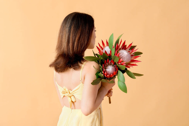 Όμορφη νεαρή γυναίκα με λουλούδια Protea στο φόντο χρώμα - Φωτογραφία, εικόνα