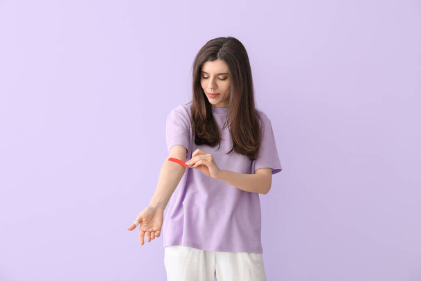 Young woman removing medical patch against color background - Photo, Image