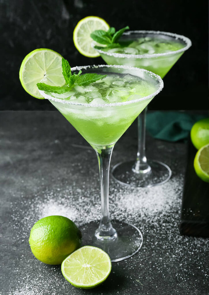 Glasses of cold daiquiri cocktail and limes on dark background - Фото, изображение