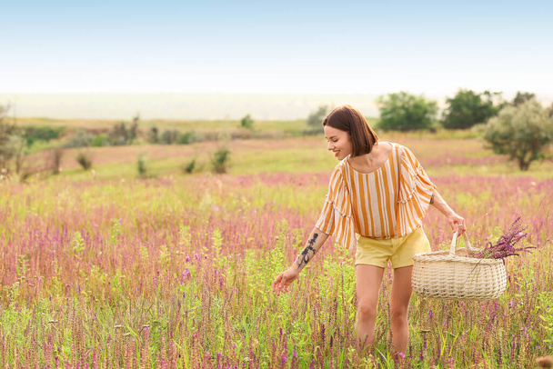 Beautiful young woman with flowers in basket on summer day - Photo, Image