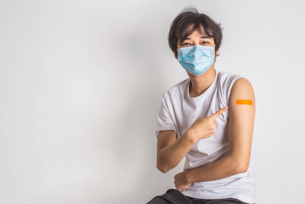 Asian man wearing face mask with a smile on his face showing his vaccinated arm. vaccination, recommended inoculation concept. - Fotó, kép