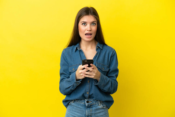 Молодая белая женщина, изолированная на желтом фоне, удивлена и отправляет сообщение - Фото, изображение
