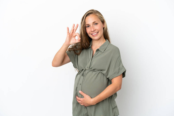 Молодая белая женщина изолирована на белом фоне беременной и делает ОК знак - Фото, изображение