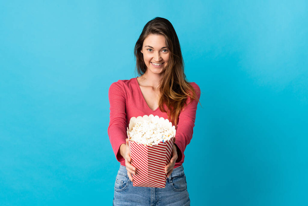 Junge Irin isoliert auf blauem Hintergrund mit einem großen Eimer Popcorn - Foto, Bild