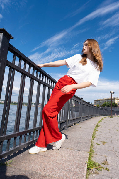 Emotional girl in bright clothes posing near the embankment hedge - Fotó, kép