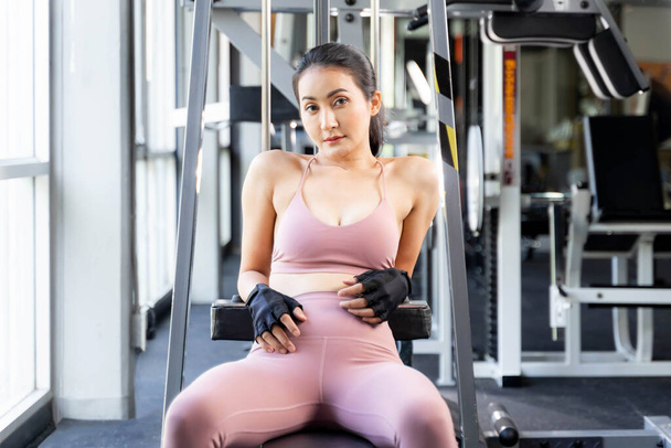 Beautiful fitness slim fit woman in sportswear sitting take a break on fitness machine in a gym room , Asian sexy girl slim body - lifestyle Healthy woman fitness concept - Photo, Image