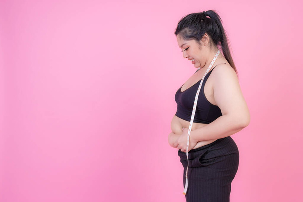 asian fat women , Fat girl , Chubby, overweight squeeze belly fat with measure tape on her neck on pink background - Woman diet lifestyle overweight problem concept - Fotografie, Obrázek