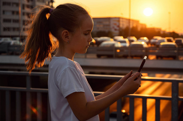 Girl types on smartphone and poses for selfie at sunset - Foto, Bild