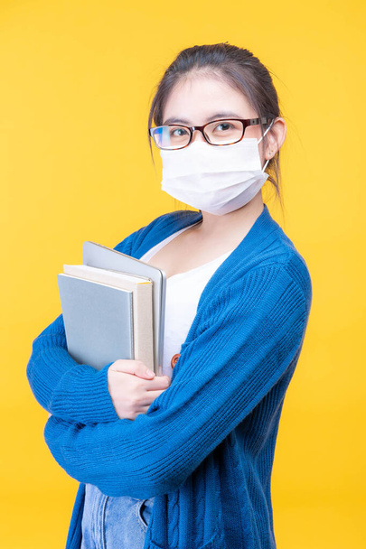 Portrait of a beautiful young woman student wear a mask holding textbook  - studying online e-learning system during the corona virus covid19 outbreak - Фото, изображение