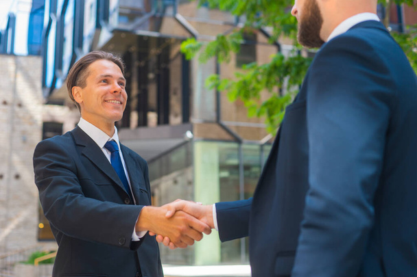 Confident businessman and his colleague are shaking hands in front of modern office building. Financial investors outdoor. Banking and business. - Zdjęcie, obraz