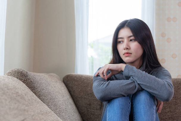 Boldogtalan ázsiai csinos fiatal nő ül egyedül kanapén érzés szomorúság - Fotó, kép