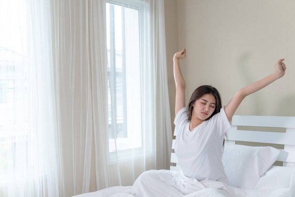 Ázsiai fiatal gyönyörű nő nyújtózkodik az ágyban, miután felébredt reggel, másolja tér - Fotó, kép